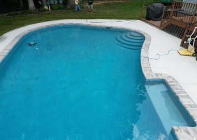 A backyard in-ground swimming pool with steps, a small attached spa, and two people in the background.