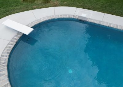 A swimming pool with a diving board and surrounding concrete deck, bordered by green grass.