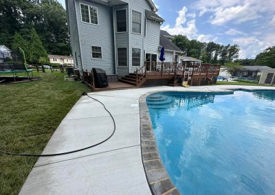 Backyard with a pool, wooden deck, grill, trampoline, and a house with gray siding under a partly cloudy sky.