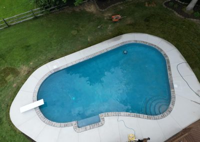 A backyard in-ground swimming pool with a diving board, surrounded by grass and a wooden fence.