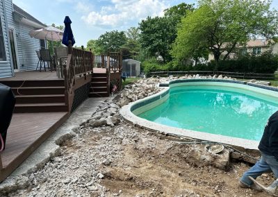 Backyard pool area under construction with broken concrete around the pool and a wooden deck nearby.