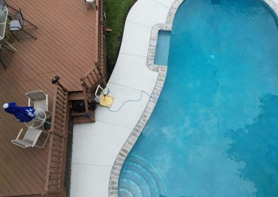 A yellow extension cord runs from a wooden deck to the edge of a swimming pool.