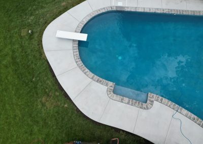 Aerial view of a swimming pool with a diving board, surrounded by grass and concrete.