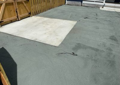 A concrete patio with a wooden fence and a section of lighter concrete near a porch.