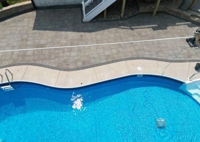 Aerial view of a blue swimming pool with a curved edge next to a stone patio and stairs.