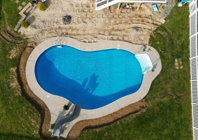 Aerial view of a kidney-shaped backyard swimming pool with a slide and surrounding patio.