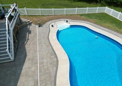 A backyard pool with blue water, surrounded by a white fence and a gray stone patio.