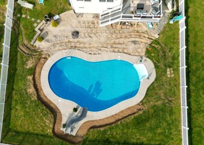Aerial view of a backyard with an irregular-shaped pool, patio, and white fence surrounding the yard.