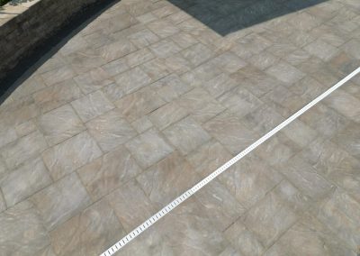Light brown stone patio with a white drainage grate running diagonally across the surface.