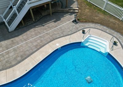 A backyard pool with white steps, surrounded by a patio and a white fence, viewed from above.