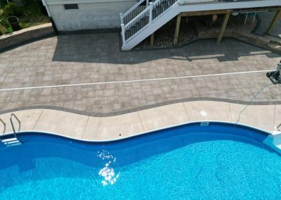 A backyard pool with curved concrete edges and a raised patio with stairs and railing in the background.