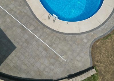 Aerial view of a round swimming pool with a curved stone patio and a metal pool ladder.