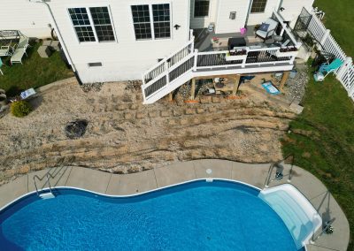 A backyard with a pool, patio, and visible dirt tire tracks leading up to a white house.
