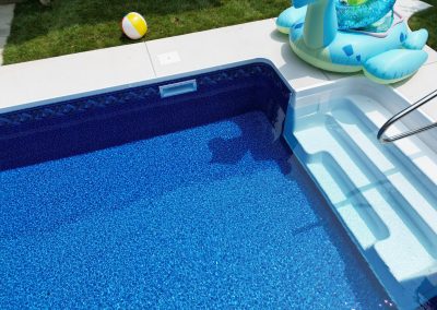 A pool with steps, a float shaped like a turtle, and a beach ball on the grass nearby.