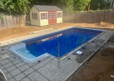 A rectangular inground pool under construction in a backyard with a yellow and red shed nearby.