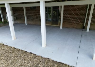 Concrete patio with white pillars and a sliding glass door, next to a brick wall.