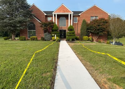 A two-story brick house with a sidewalk bordered by yellow caution tape on a grassy lawn.