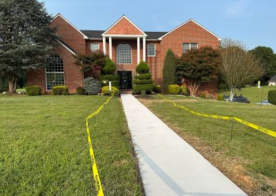 A brick building with new sidewalk, lined by yellow caution tape, on a grassy lawn.