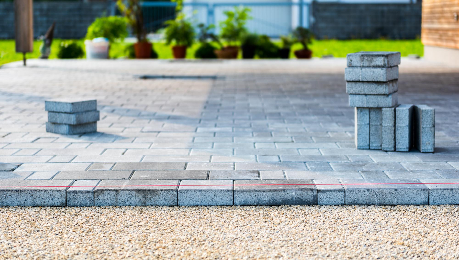 15285237 Stacks of gray paving stones on a partially completed patio with plants and grass in the background.