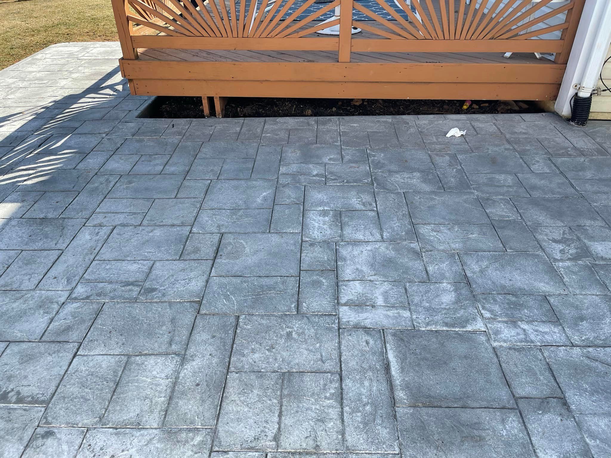 Gray patterned stone patio with a wooden deck and decorative railing in the background.